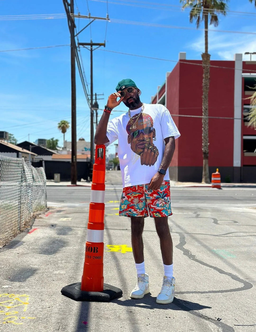 Person wearing a white t-shirt with a graphic design and colorful shorts standing next to traffic cones on a street.