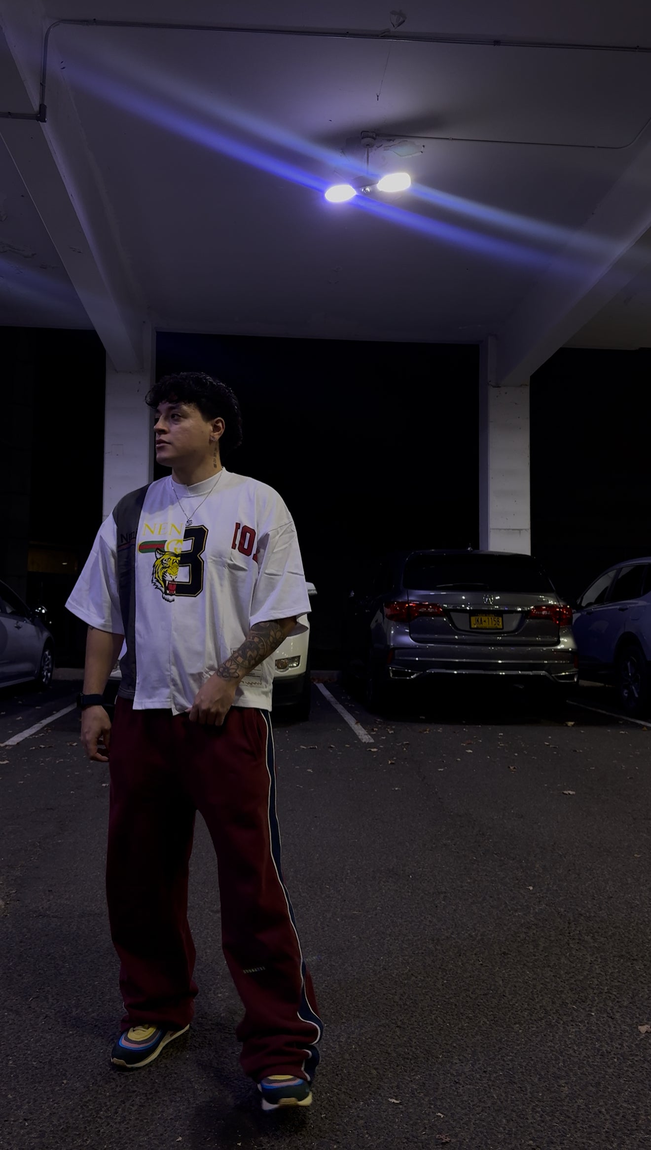 Person standing in a dark parking lot with cars in the background, streetwear shirt, uneven. y2k shirt