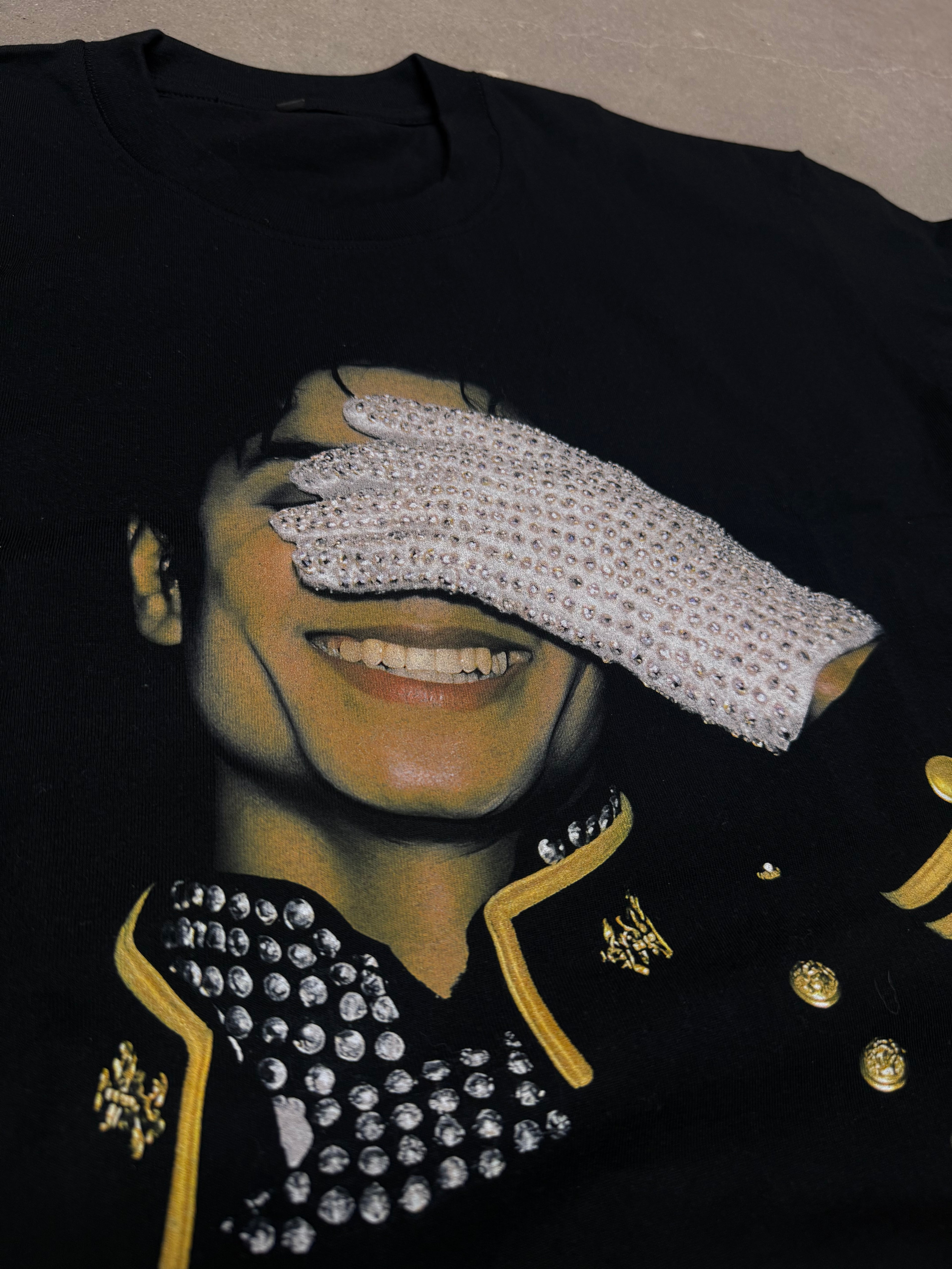 Black garment with decorative elements including a white glove, gold accents, and a patterned design. michael jackson graphic shirt