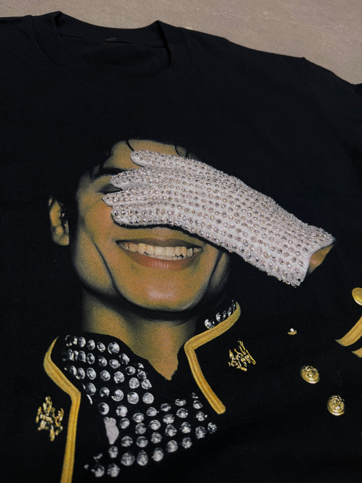 Black garment with decorative elements including a white glove, gold accents, and a patterned design. michael jackson graphic shirt