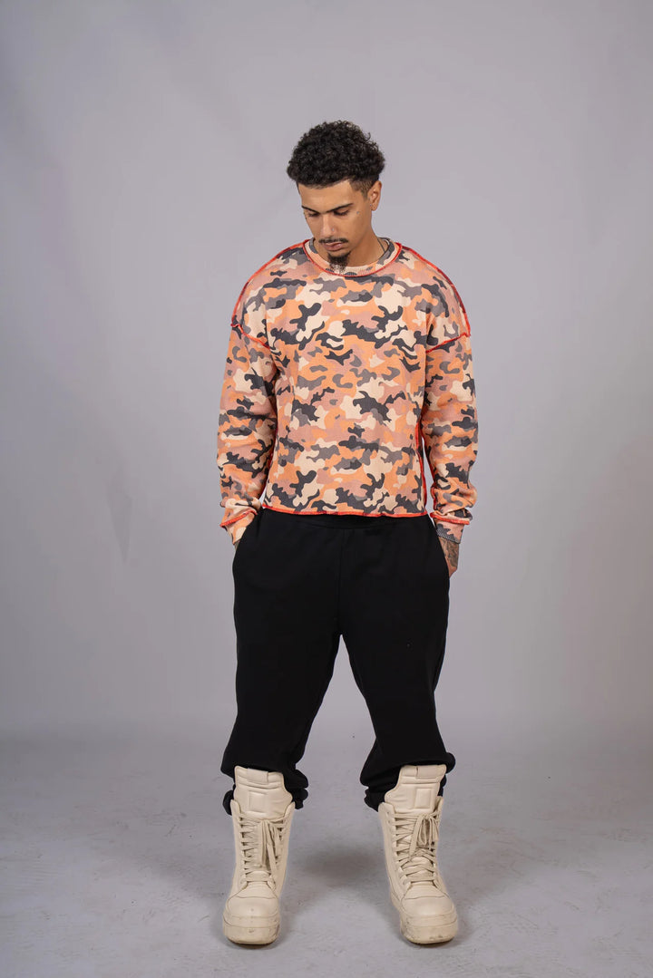 Person wearing a camouflage sweatshirt and black pants on a gray background