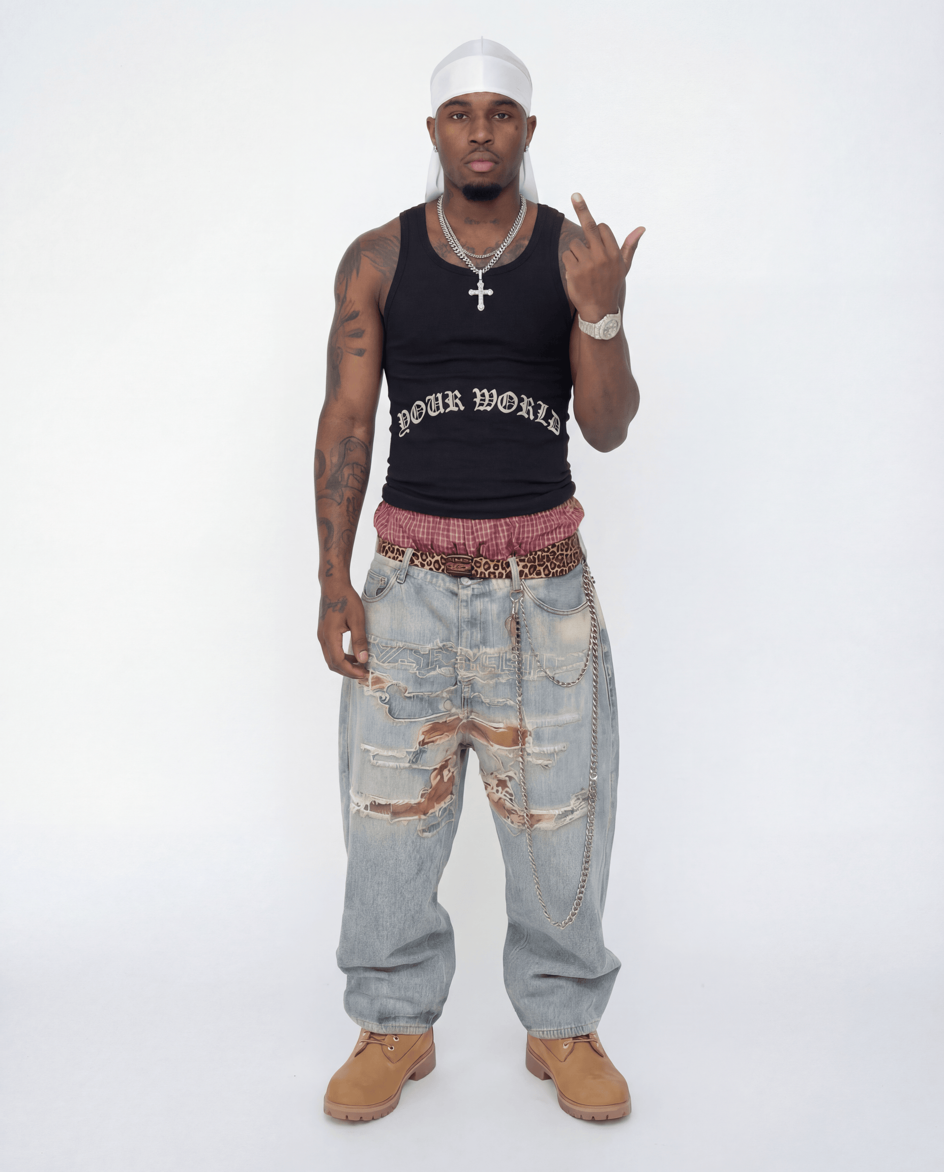 Man wearing a black tank top with text, light blue jeans, and tan shoes on a white background