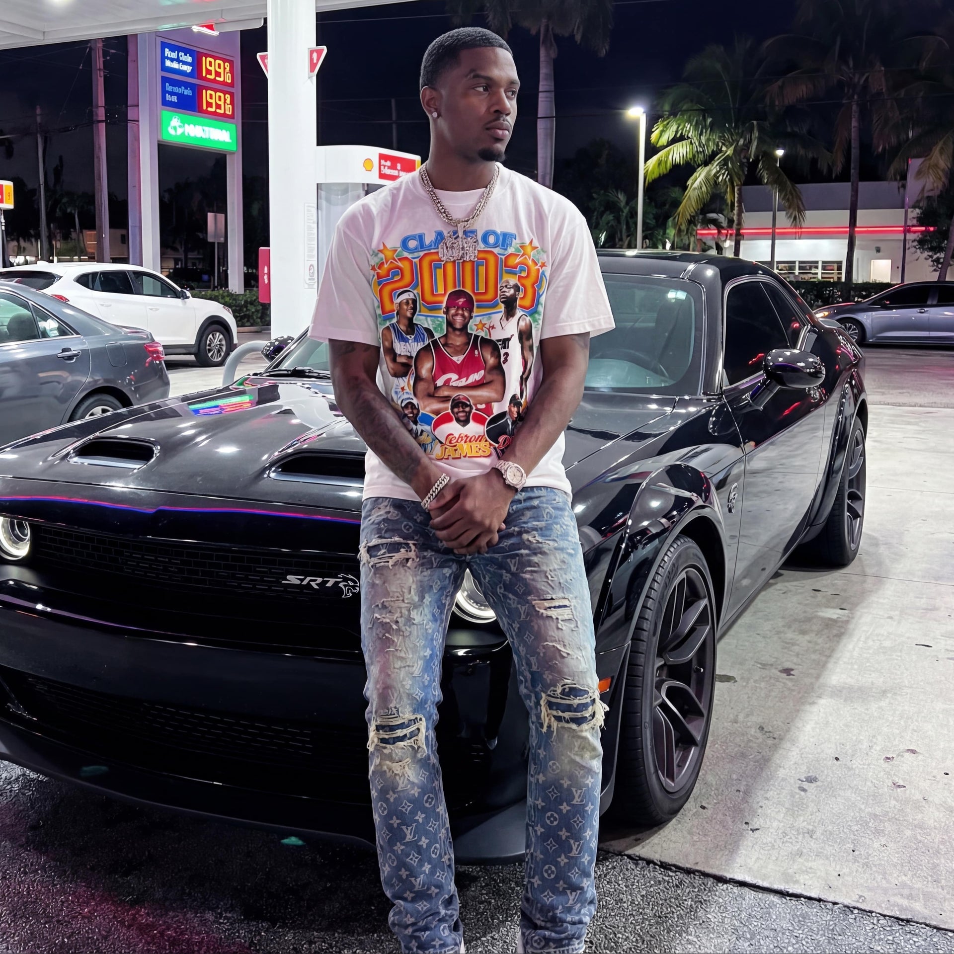 Man standing next to a black muscle car at a gas station